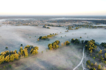 Mist covers the river, trees, and land at dawn. Autumn photos of fog taken with drone