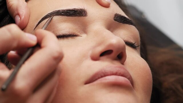 Eyebrow coloring. Professional lamination procedures of female eyebrows in beauty salon. Closeup view of client face and stylist's hands working. 4K Cinematic footage.