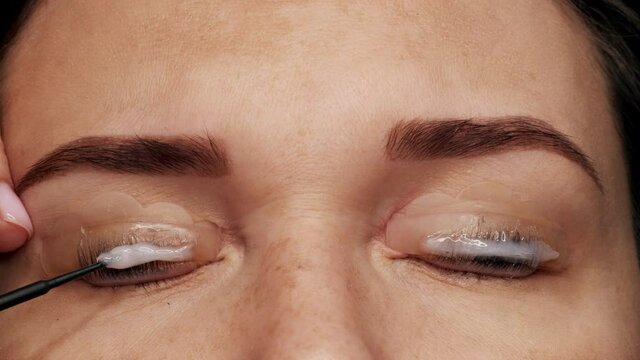 Woman face on modern eyelash lamination procedure in a professional beauty salon. Master applies special glue before the eyelash curling procedure, close up. Beauty salon.