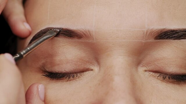 Eyebrow coloring. Professional lamination procedures of female eyebrows in beauty salon. Closeup view of client face and stylist's hands working. 4K Cinematic footage.