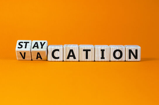 Vacation or staycation symbol. Turned wooden cubes and changed the word vacation to staycation. Business and vacation or staycation concept. Beautiful orange background, copy space.