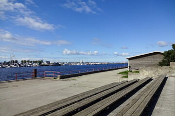 Fototapeta na wymiar Wood from wooden benches to Pirita river coming into the sea. Seaview with yachts and boats on a dock on a sunny day with blue sky. Pirita, Tallinn, Estonia, Europe. September 2021