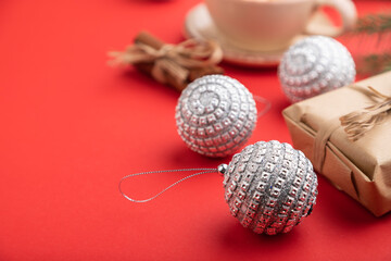 Christmas or New Year composition. Decorations, silver balls, fir and spruce branches, cup of coffee, on a red background. Side view, selective focus.
