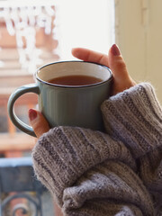 Manos de chica con jersey sujetando una taza caliente en un día de invierno.