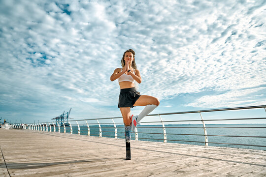 Image of a strong healthy young disabled sportswoman make yoga exercise on a bridge near sea.