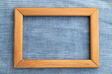 Wooden frame on smooth blue linen tissue. Top view, natural textile background.