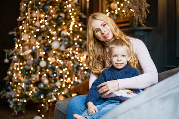 Fototapeta na wymiar Happy mom and son are sitting on the sofa against the background of a decorated festive christmas tree
