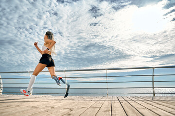 Take care of your body. Side view of a strong disabled woman in sportswear with a prosthetic leg is...