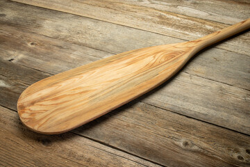 blade of wooden canoe paddle against rustic weathered wood