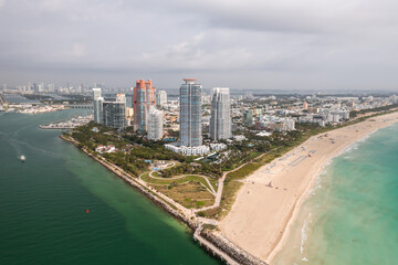 Obraz premium Incredible daytime aerial view of South Pointe high-rise condominiums looking down Miami Beach with sandy shores lining the turquoise waters of the Atlantic Ocean with cloudy sky above.