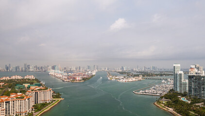 Incredible aerial view over the Miami shipping channels with the skyline on the horizon beyond and cloudy sky above as boats and ferries make their way to and from Fisher Island below.