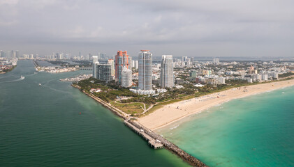 Fototapeta na wymiar Incredible daytime aerial view of South Pointe high-rise condominiums looking down Miami Beach with sandy shores lining the turquoise waters of the Atlantic Ocean with cloudy sky above.