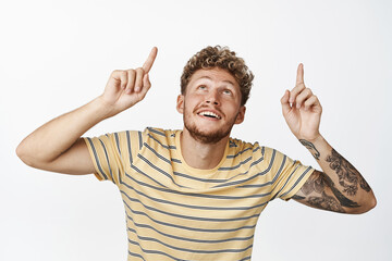 Handsome blond smiling man pointing fingers up, bending while looking up with excited face...