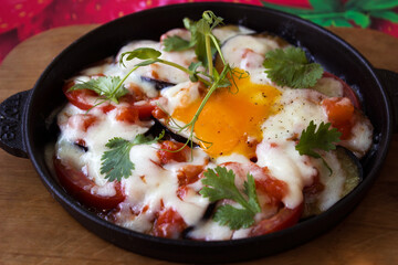 Breakfast at a street cafe. Fried eggs with vegetables (with tomatoes, eggplant and herbs) served in a frying pan