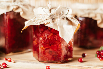 Jars of homemade lingonberry and pear jam with craft paper on lids on wooden table next to fresh lingonberries and pears