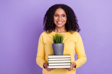 Photo of charming sweet dark skin girl dressed yellow sweatshirt glasses holding book stack plant isolated purple color background