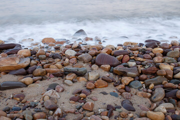 soft blue waves coming through colourful pebbles at the beach in Adelaide, South Australia