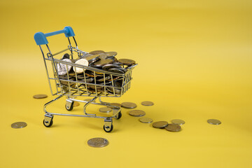 Mini shopping basket with coins in yellow background. Finance and the concept of saving money