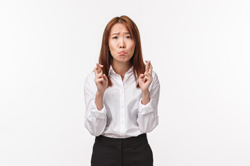 Miserable and desperate cute asian woman cross fingers good luck, nervously and impatiently looking...