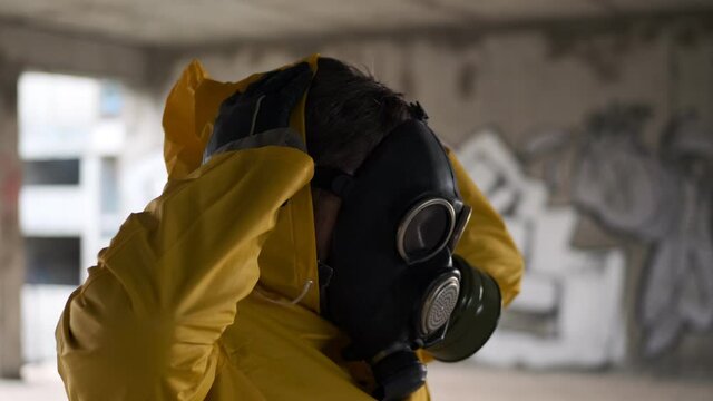Post Apocalypse, man in abandoned building takes off his gas mask and breathes deeply, breathing freely. stalker in yellow protective suit takes off his mask, air is clean, you can live.