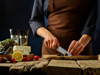 The chef is cutting olives on a wooden cutting board. Greek salad. The classic recipe. Ingredients. Vitamins, diet food. Restaurant, hotel, cafe, menu design.