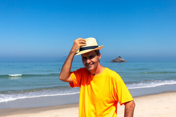 Fototapeta na wymiar man wearing Panama hat in an orange T-shirt on the beach, smiling at the camera