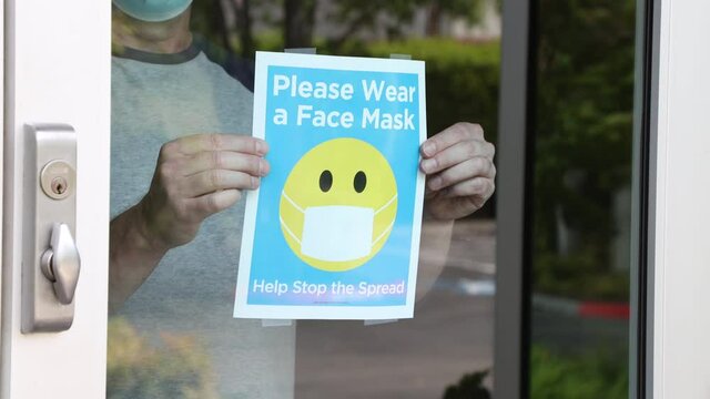 male shop owner wearing a face mask posts a notice on the glass door entrance requi