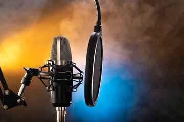 Studio professional microphone and pop filter on yellow-blue smoky background. There are no people...