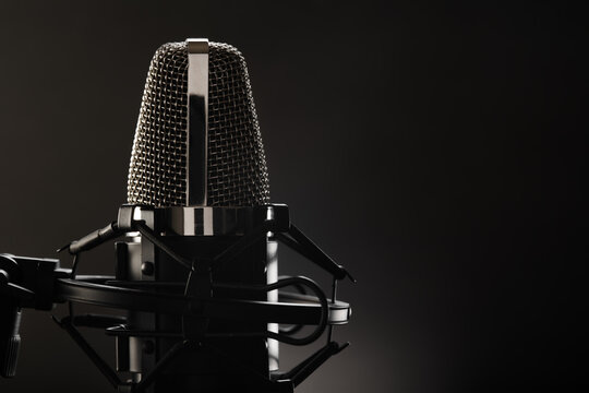 One professional studio microphone on a dark gray background. Close-up. There are no people in the photo. Monochrome image. Singing, speaking, concert, debate, purity of sound.