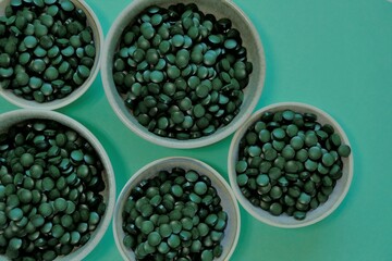 Spirulina algae dry tablets. Spirulina pills in cups on a green background. Vegetarian omega...