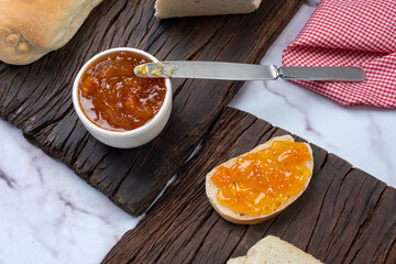 snack or breakfast with homemade sweet fruit jam in white bowl with slices of homemade bread on wooden board