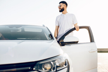 young handsome man in sunglasses posing near a car in the city center