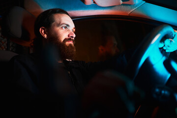 Confident bearded man driving inside his vehicle at night