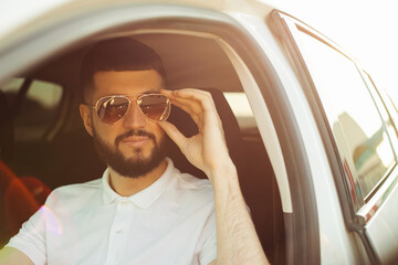 Naklejka premium young man with beard wearing sunglasses smiles while driving a car