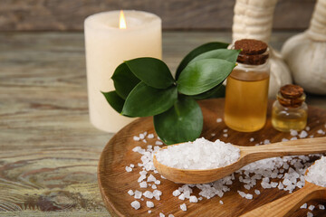 Beautiful spa composition with sea salt and bottles of essential oil on wooden background, closeup