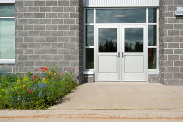 Double commercial exterior steel doors of a business. The glass is on top, trim is stainless steel metal. The doors have metal handles. There are large grey brick walls on both sides of the doors. 