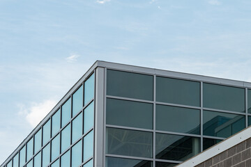 Exterior corner of a commercial building with glass windows reflecting the sky and a dark brown...