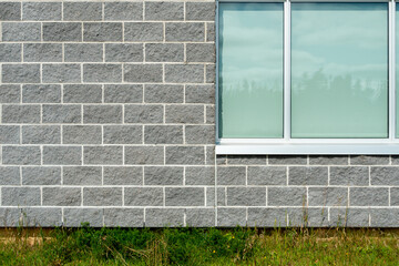 The exterior of a commercial building is built of grey stone brick with white mortar. There's a multi glass pane window with stainless steel trim surrounding the glass. The foreground is green grass. 