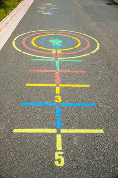 A colorful outdoor children's recreation game that has multiple lines and circles painted on asphalt in a school park or playground. There are numbers painted on the lines from one to five. 