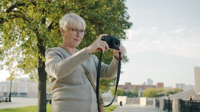 Mature woman tourist is taking pictures of beautiful city using professional camera on summer day enjoying creative activity. People and photography concept.