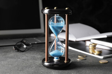 Stylish hourglass and laptop on dark table in office. Deadline concept