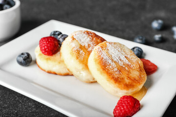 Plate with tasty cottage cheese pancakes, berries and honey on dark background, closeup