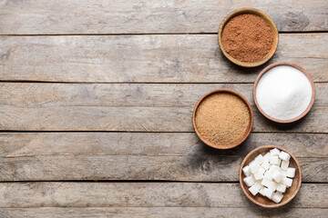 Bowls with different sugar on wooden background