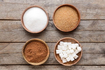 Bowls with different sugar on wooden background