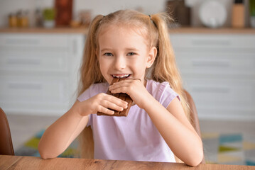 Cute little girl eating sweet chocolate in kitchen