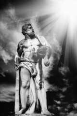 Fototapeta na wymiar Ancient stone statue of Hercules against dramatic view of cloudy sky as symbol of power and strength.. Black and white vertical image.