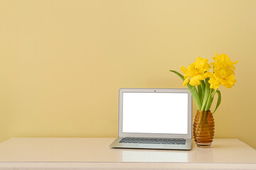 Stylish workplace with modern laptop and flowers near light wall