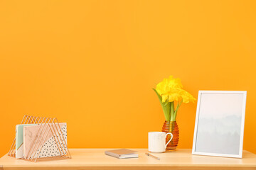 Stylish workplace with beautiful flowers, cup of coffee and notebooks near color wall