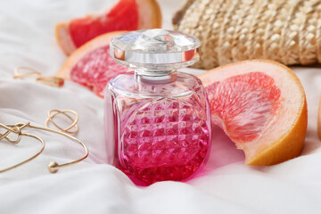 Bottle of perfume and grapefruit on white cloth background, closeup