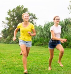Two young barefoot girls in shorts running on meadow together.